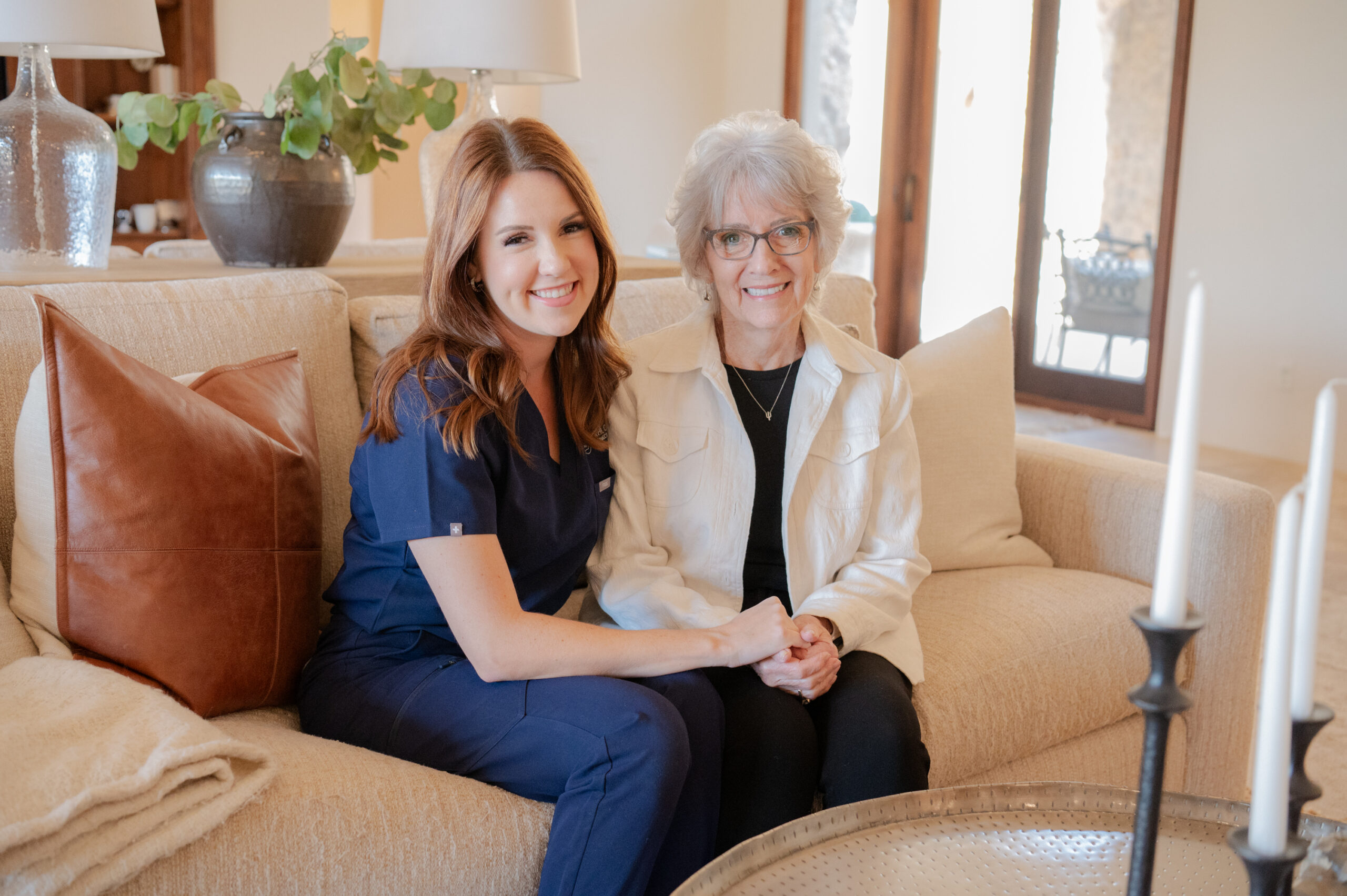 A caregiver from Total Care Connections and a senior client sitting on a sofa, smiling at the camera.